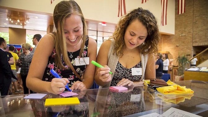 Two students write on sticky notes