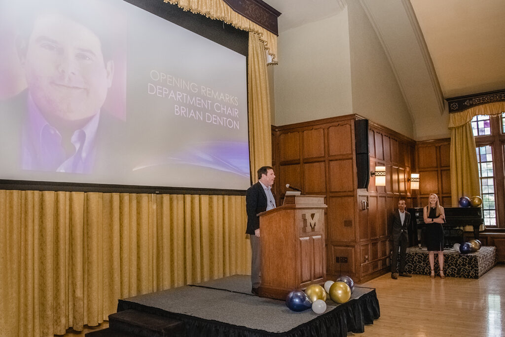 Brian Denton stands on stage and speaks to a room full of people