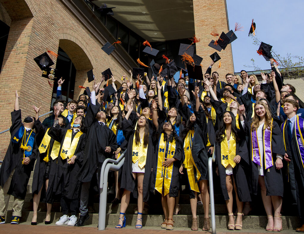 Students in graduation robes throw their caps in the air