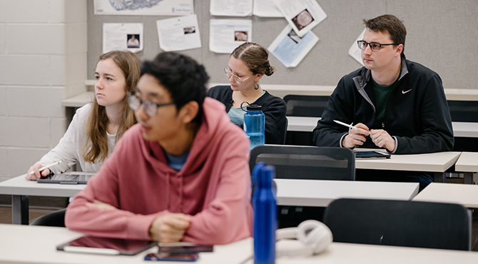 Four students watch a professor teach