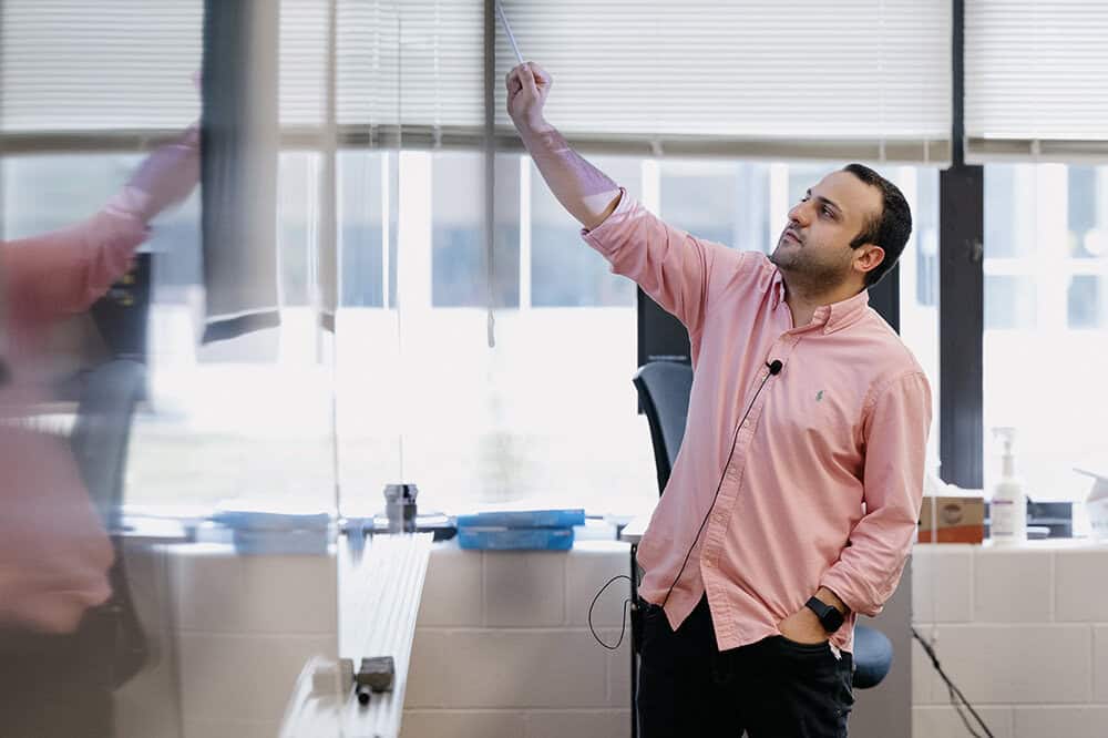 Raed Al Kontar points at a white board with a marker while he is teaching in a classroom setting