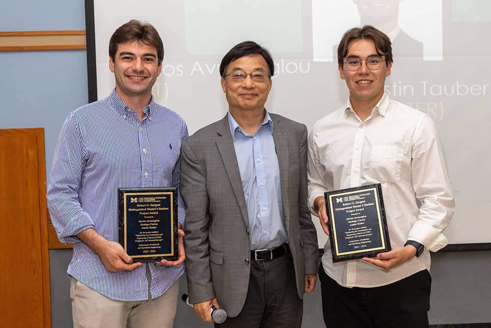 Three people smile for a photo while two hold award plaques