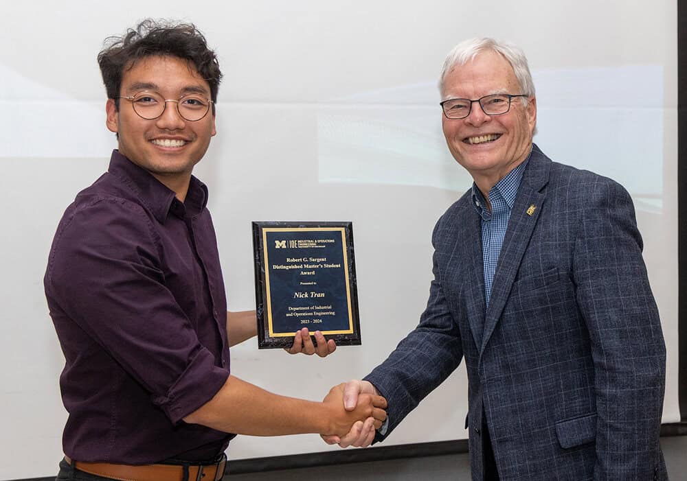 Two people shake hands while one holds an award plaque