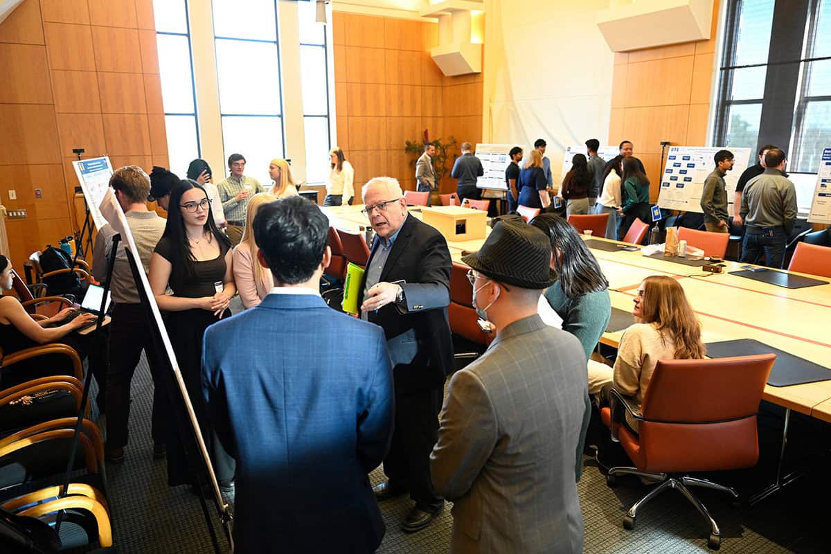 Many people stand in a crowded room looking at research posters