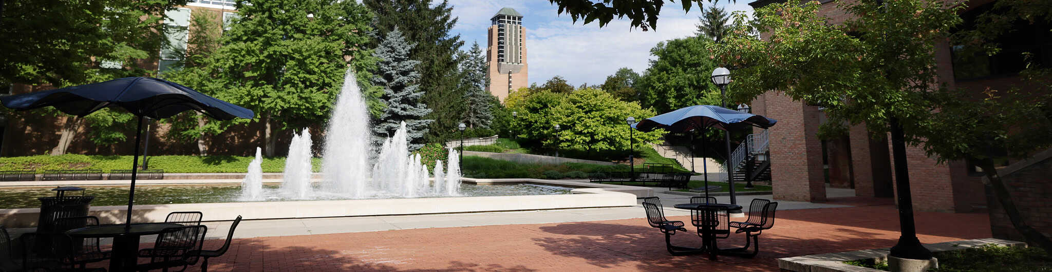 Large water fountain with table and umbrellas placed around it. 